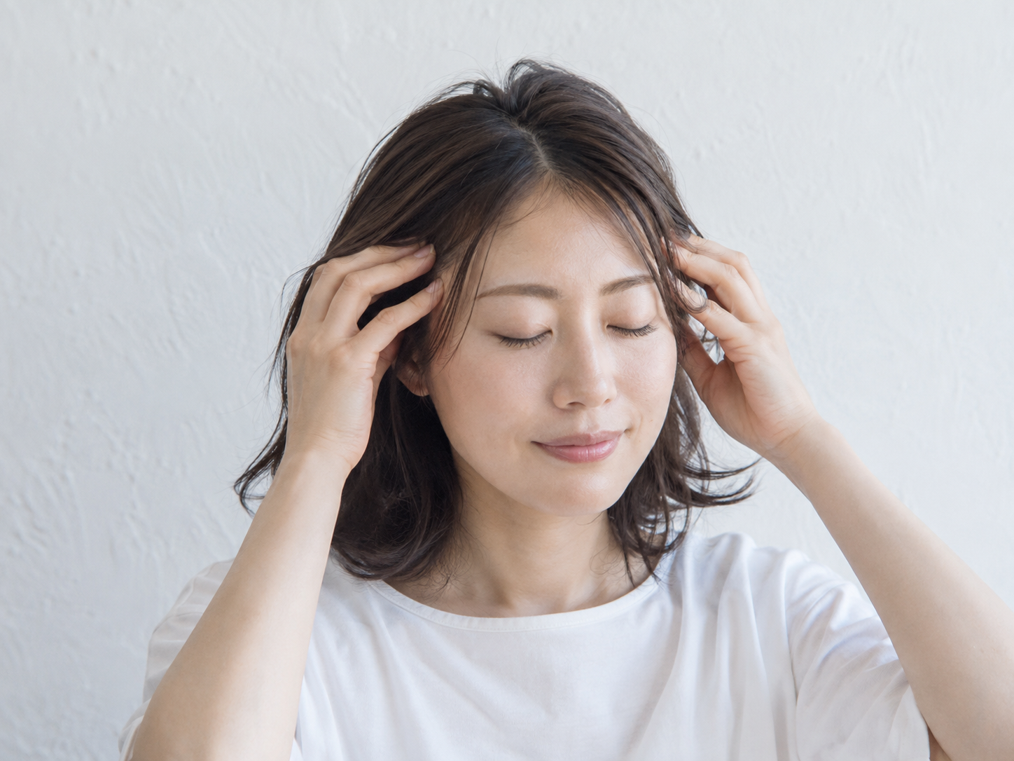 指の腹をこめかみ付近の頭皮へ軽く当てるセルフケアの様子